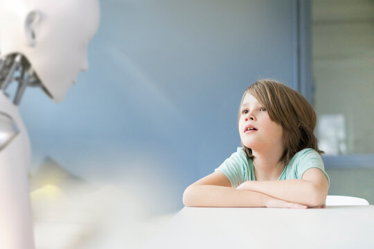 Little boy sitting at table, talking to a robot
