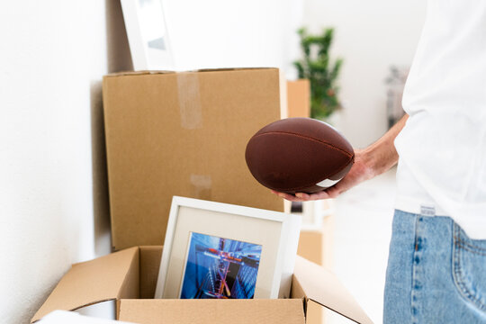 Man holding rugby ball in hand while unpacking in new apartment