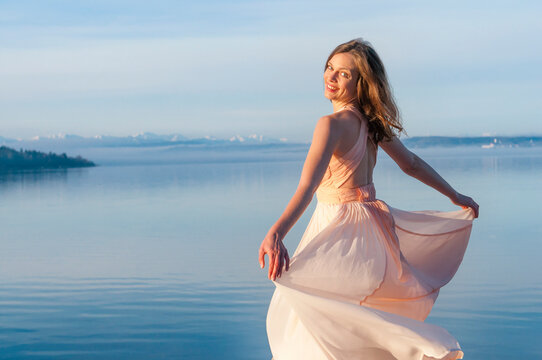 Rear view portrait of smiling beautiful woman in dress standing at lakeshore on sunny day