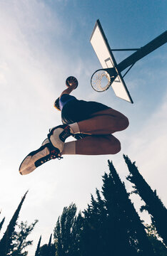 Directly below view of teenage player dunking ball in basketball hoop against sky