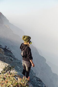 Young woman with respirator mask standing at the edge of volcano Ijen, Java, Indonesia