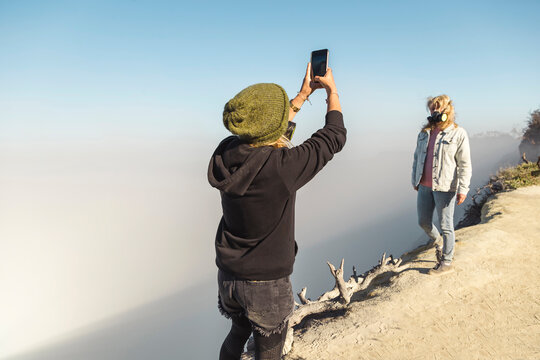 Young woman with respirator mask taking a photo of her girlfriend at the edge of volcano Ijen, Java, Indonesia