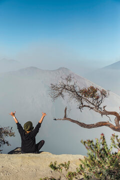 Woman with respirator mask sitting at volcano Ijen and  raising her arms, Java, Indonesia