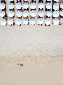 Indonesia, Bali, Aerial view of man sunbathing in front of rows of beach umbrellas on sandy coastal beach of Nusa Dua