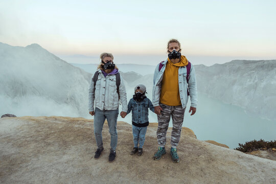 Family with respirator masks standing hand in hand at the edge of volcano Ijen, Java, Indonesia