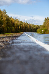 Straight road with a marking on the nature background. Open Road in future, no cars, auto on asphalt road through green forest, trees. Clouds on blue sky in summer, sunshine, sunny day. Bottom view