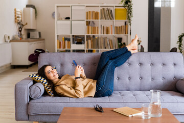Smiling woman using smart phone while sitting on sofa at home