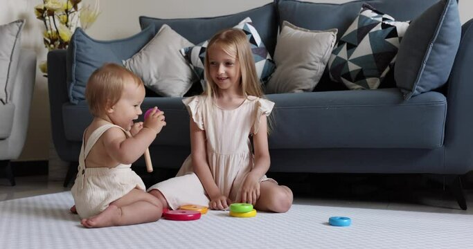 Two cute little caucasian children siblings playing together with wooden toys on floor at home. Children development concept. Infant baby girl with blonde hair plays with elder sister. Slow motion 4k