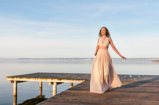 Full length of smiling beautiful woman walking on pier over lake against sky