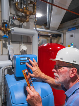 Senior craftsman checking water-processing unit, reading tablet