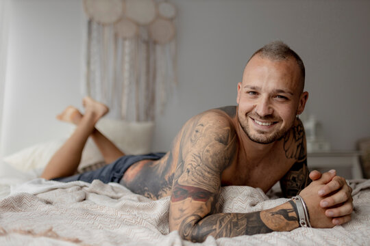 Handsome man with tattoo on arm lying on bed