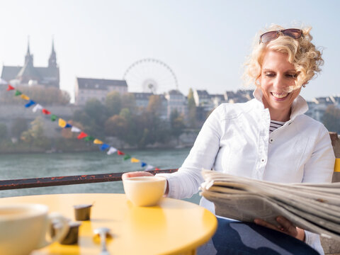 Switzerland, Basel, smiling woman reading newspaper in a street cafe at River Rhine