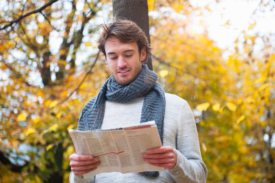 Portrait of young man reading newspaper outdoors