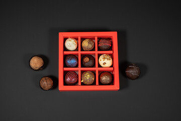Various handmade chocolate truffle candies in a red box on a dark background. Directly above top view.