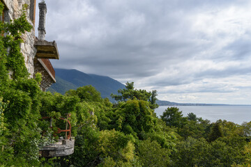 View of the park, mountains and the Black Sea from the balcony of the abandoned castle of the Prince of Oldenburg in Gagra (Abkhazia) in summer. Remains of a balcony overgrown with green bushes. 