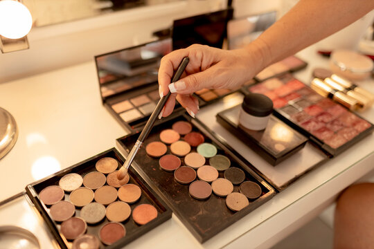 Close-up of beautician's hand with make-up brush and palettes on dressing table