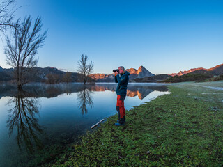 Spain, Asturias, Camposolillo, Cantabrian Mountains, senior man taking a photo at the seashore of Porma reservoir