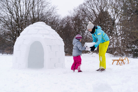 Mother helping daughter to carry snow block at park