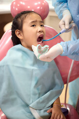 A girl is applying dental fluoride treatment. Asian girl sitting in a chair to heal her teeth. A senior pediatric dentist treats a patient's teeth at the dental office.