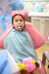 A girl is applying dental fluoride treatment. Asian girl sitting in a chair to heal her teeth. A senior pediatric dentist treats a patient's teeth at the dental office.