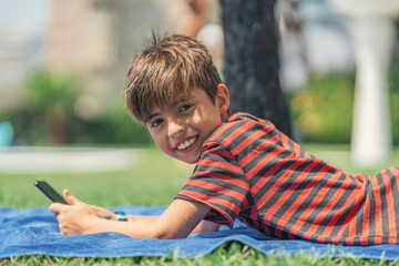 Smiling boy using smart phone while lying on towel in yard