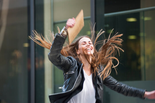 Cheerful Young Woman Holding Laptop While Jumping In City