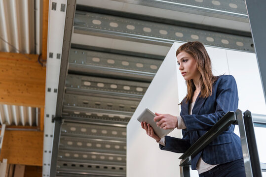 Businesswoman holding digital tablet looking away while standing by railing in factory