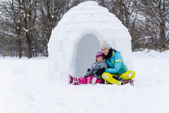 Smiling mother and daughter sitting against igloo at park