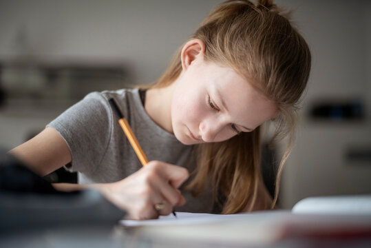 Girl learning at home, writing in exercise book
