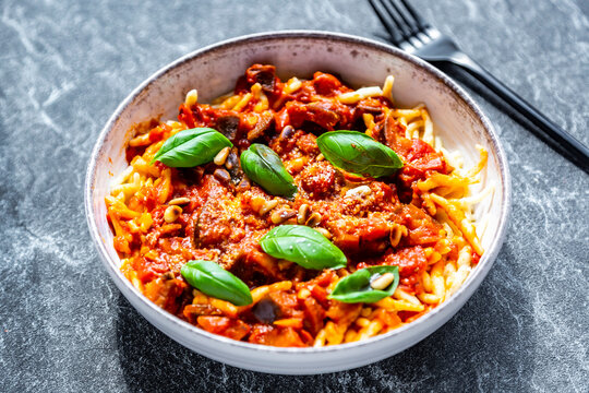 Bowl of pasta with aubergine tomato sugo garnished with pine nuts, parmesan and basil