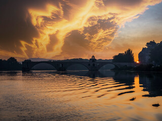 Clouds over river Rhone at sunset with silhouette of arch bridge in background, Vaucluse, France
