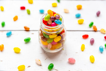 Glass of colourful sweet jellybeans on white wood