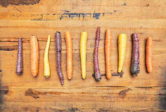 Row of purple, orange and yellow carrots on wooden surface