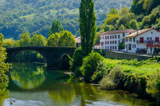 France, Pyrenees-Atlantiques, Bidarray, Arch bridge over Nive river with village houses in background