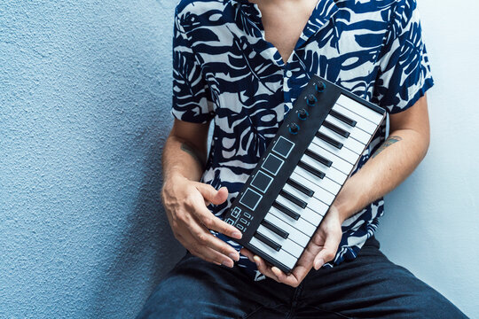 Man playing midi keyboard while sitting against wall