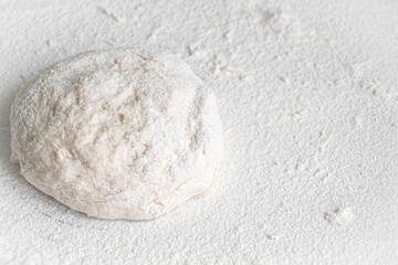 Fototapeta na wymiar Lump of yeast dough sprinkled with flour. Culinary baking background with copyspace. Yeast dough for bread, spaghetti or pizza on a rolling board. Cooking bread. Kneading dough.