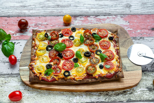 Low carb flax seed pizza with cheese, cherry tomatoes, olives and basil