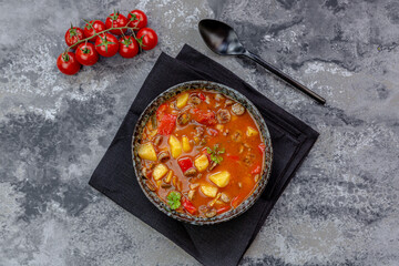 Bowl of sausage goulash with potatoes, tomatoes, bell peppers, leek and parsley