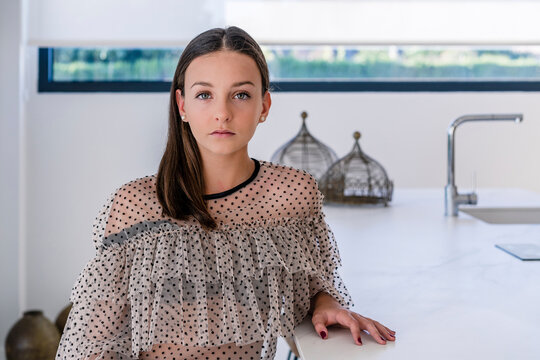 Confident teenage girl sitting by kitchen island at home
