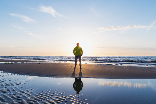Rear view of senior man standing on shore at beach during sunset, North Sea Coast, Flanders, Belgium