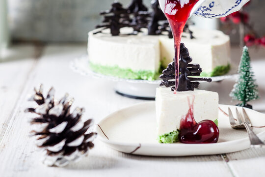 Piece of no-bake cheesecake, decorated with chocolate Christmas trees on plate with hot cherry sauce