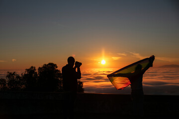 Photographer taking picture of man wrapped in a gay pride flag in backlight
