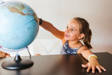 Happy schoolgirl looking at globe on desk
