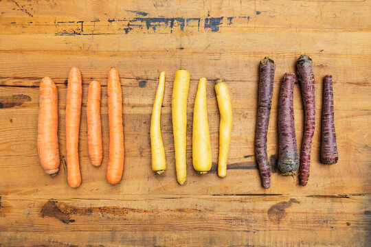Row of purple, orange and yellow carrots on wooden surface
