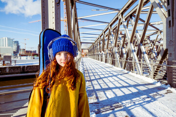 Girl with guitar listening music through headphones while standing on bridge