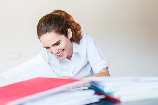 Smiling female student reading document at desk at home