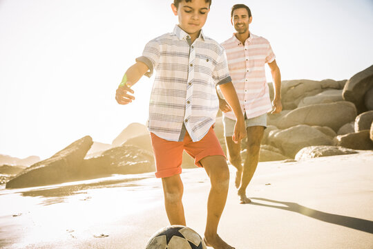 Father and son playing soccer on the beach