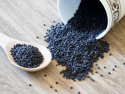 Black lentils spilling out of container lying on wooden surface