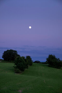 Empty grass field against full moon in purple sky