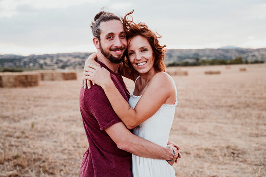 Smiling couple with arm around standing in field during sunset